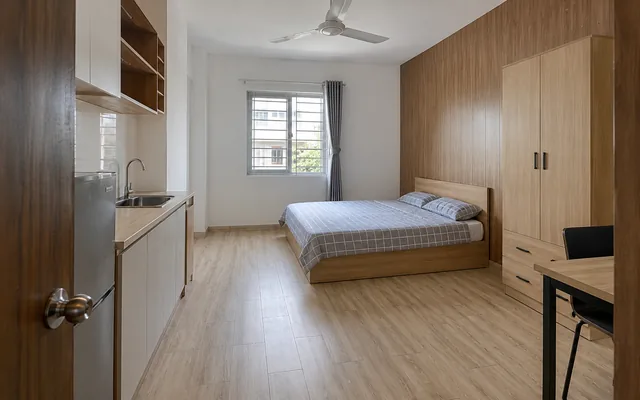 Ảnh minh họa: Phòng trọ khoảng 20 m² lát sàn nhựa vân sồi sáng, vách đầu giường ốp tấm nhựa vân gỗ nâu, có góc bếp nhỏ và quạt trần.