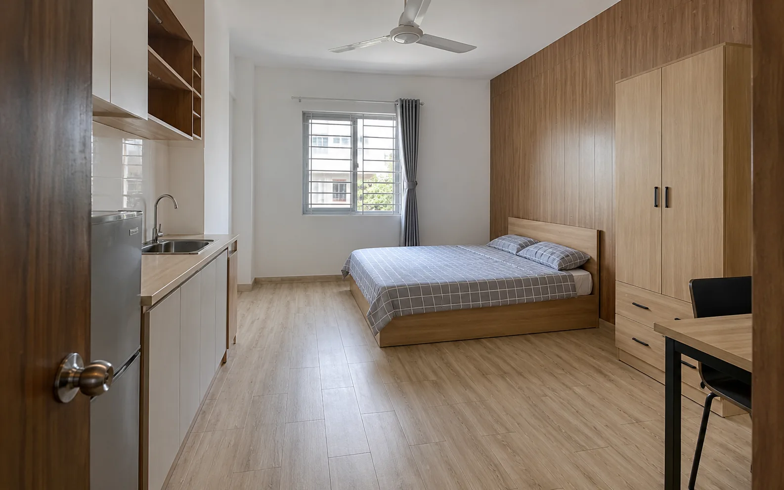 Ảnh minh họa: Phòng trọ khoảng 20 m² lát sàn nhựa vân sồi sáng, vách đầu giường ốp tấm nhựa vân gỗ nâu, có góc bếp nhỏ và quạt trần.
